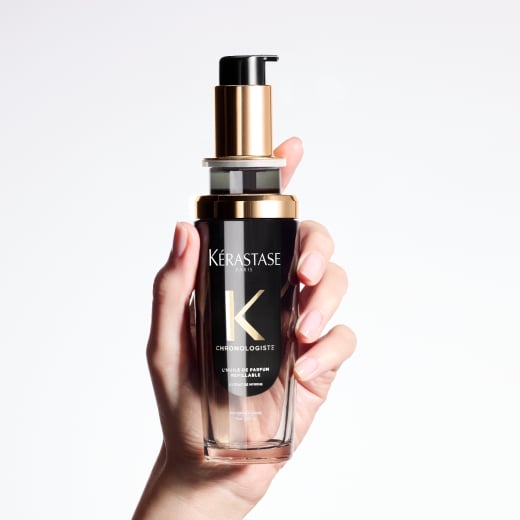  Chronologiste Huile de Parfum hair oil - featuring an artful blend of addictive fragrances mingling cedar, magnolia, and tea rose - is being held between two hands.